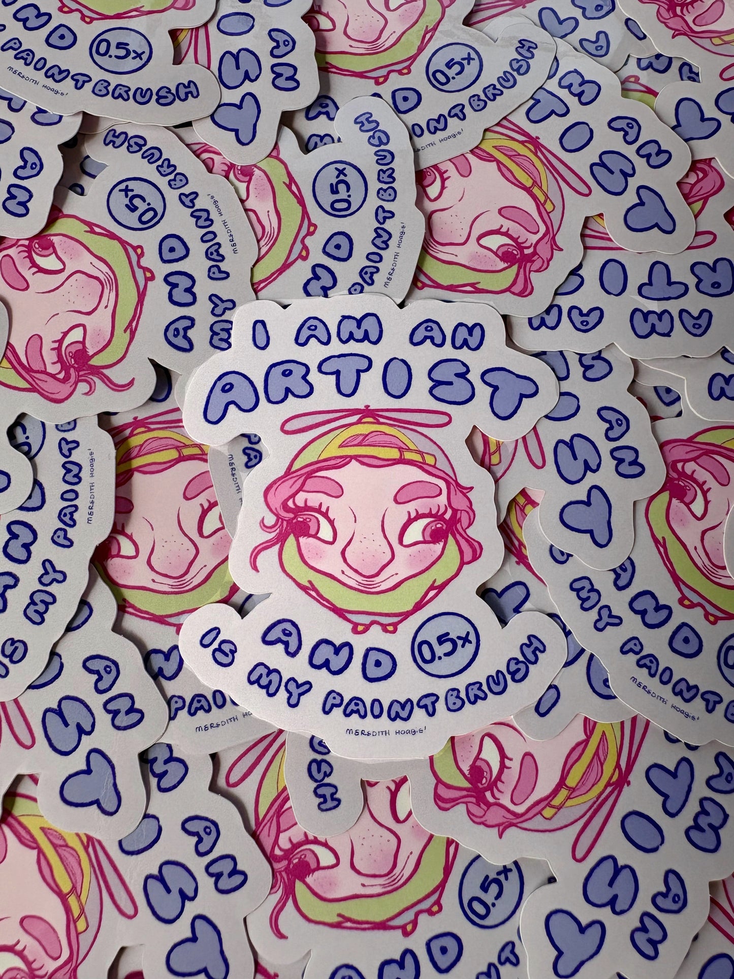 Sticker with funny fisheye lens'd face design and text 'I am an artist and 0.5x is my paintbrush' on a background of similar stickers by Meredith Hoagie