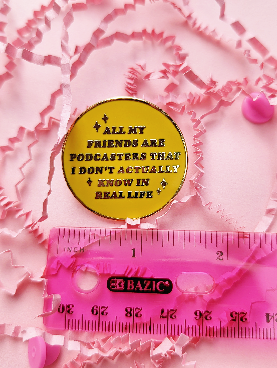 Cute Yellow Enamel Pin that says "All My Friends Are Podcasters That I Don't Actually Know In Real Life" on a pink background above a pink ruler showing it is 1.5 inches in size | Ideal of the chronically online