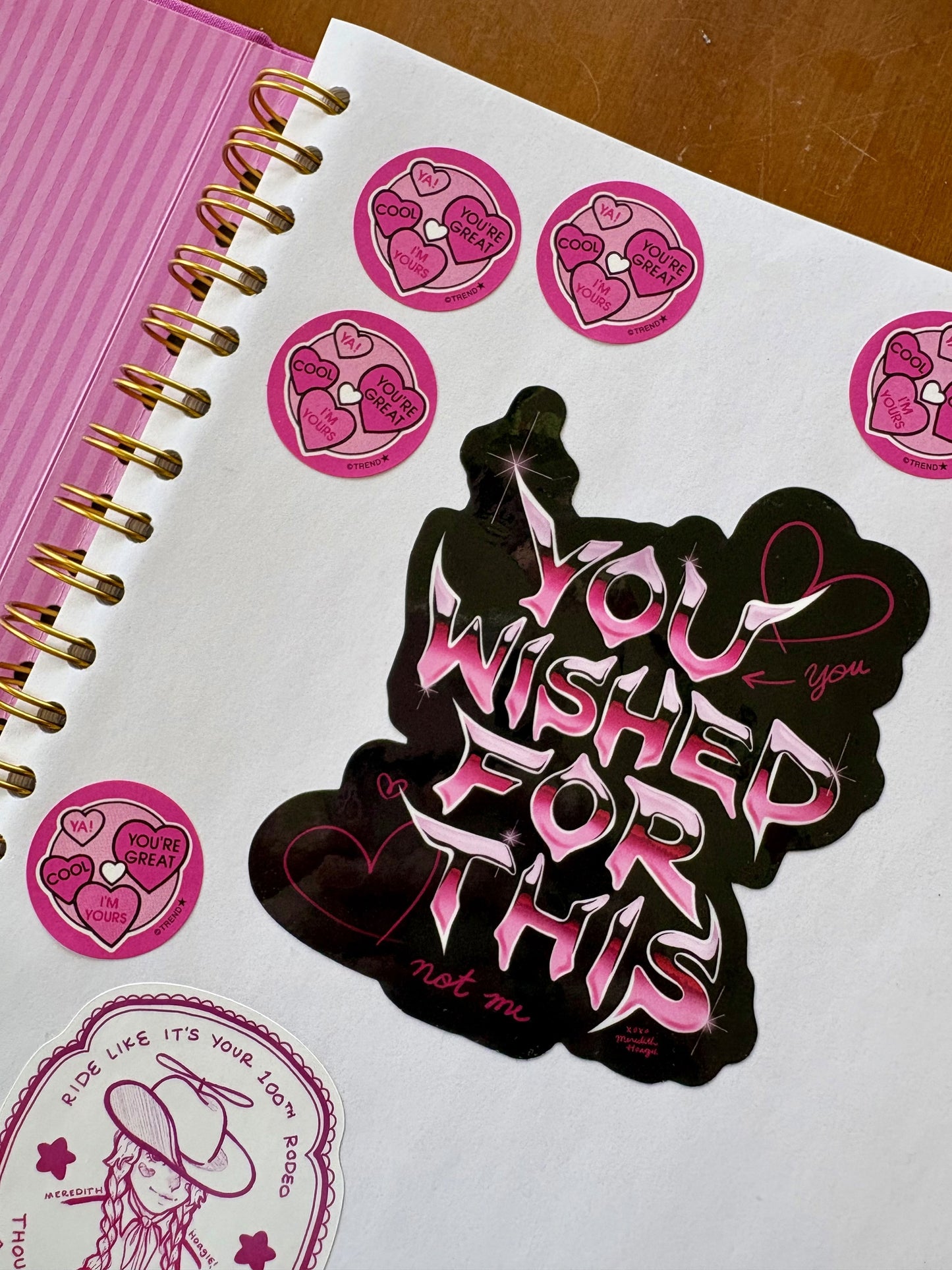Sticker with 'You wished for this, not me' text on the Coffee Table Sticker Book with pink stickers by Meredith Hoagie