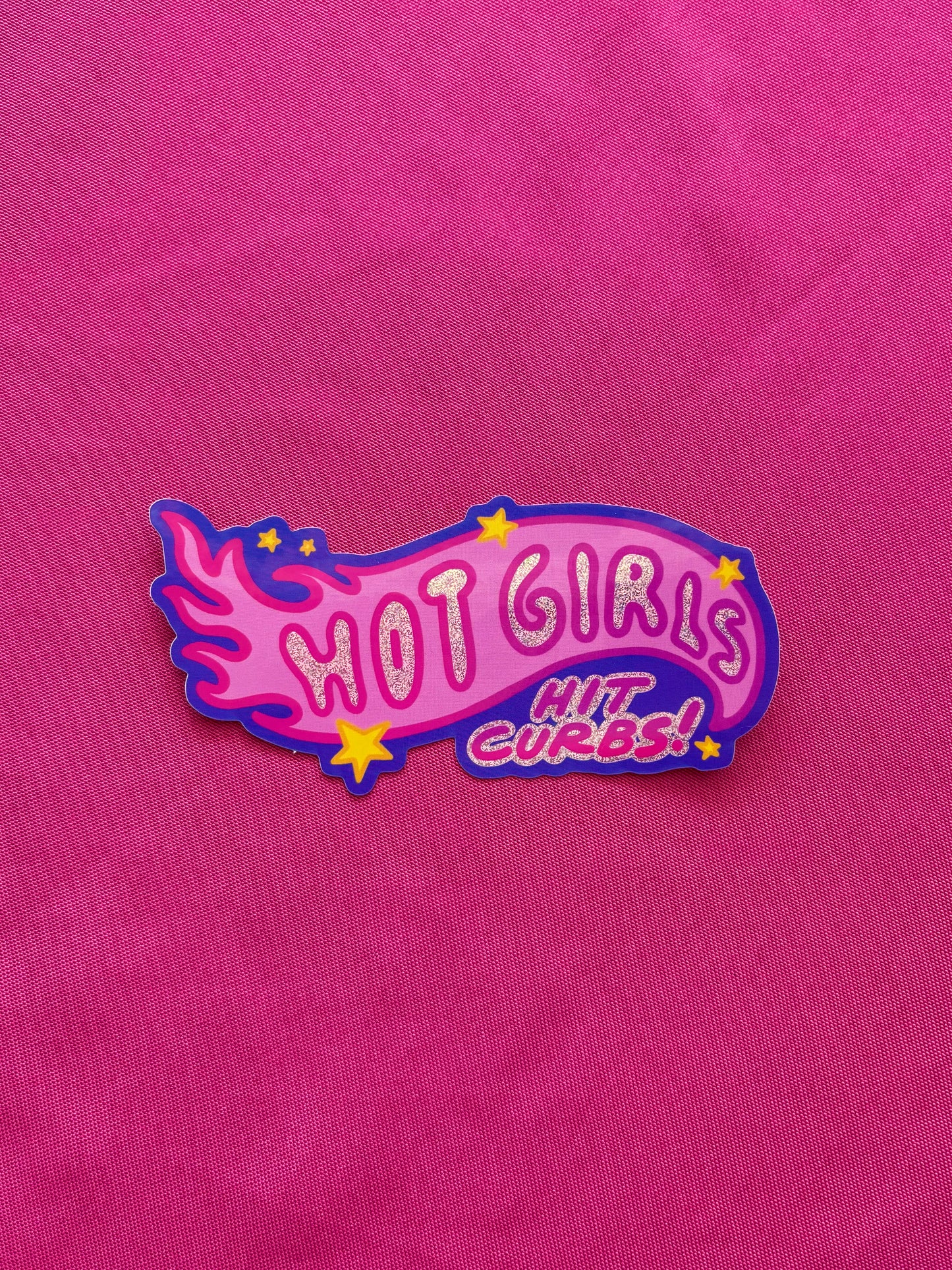 Pink die cut sticker with 'HOT GIRLS HIT CURBS!' text on a pink tablecloth