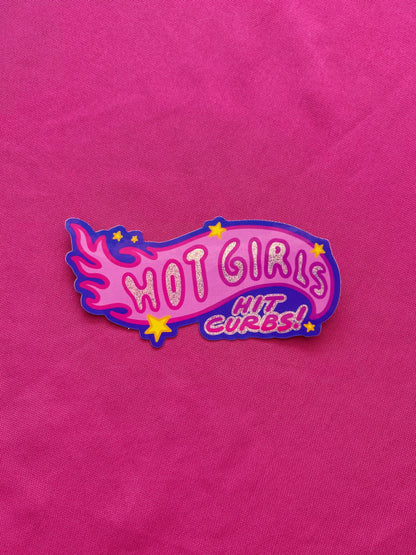 Pink die cut sticker with 'HOT GIRLS HIT CURBS!' text on a pink tablecloth