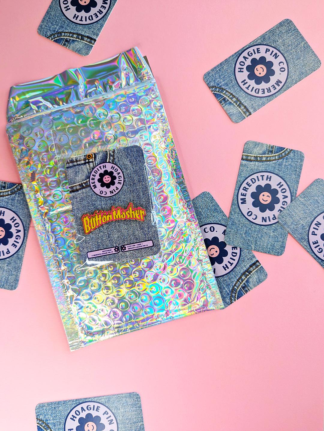 button masher gaming enamel pin with packaging on pink background
